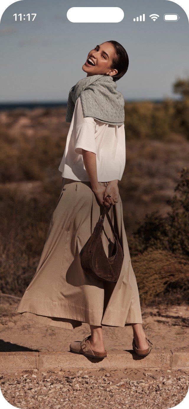 a woman walking down a dirt road with a purse