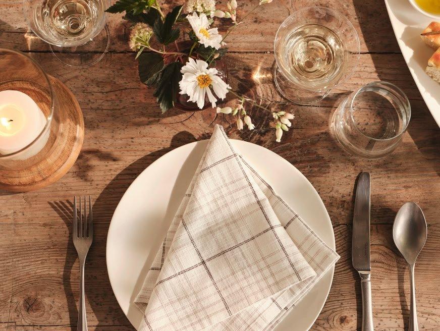 a table with a white plate, silverware, napkin and flowers