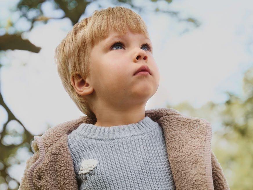a young boy wearing a sweater and looking up at the sky