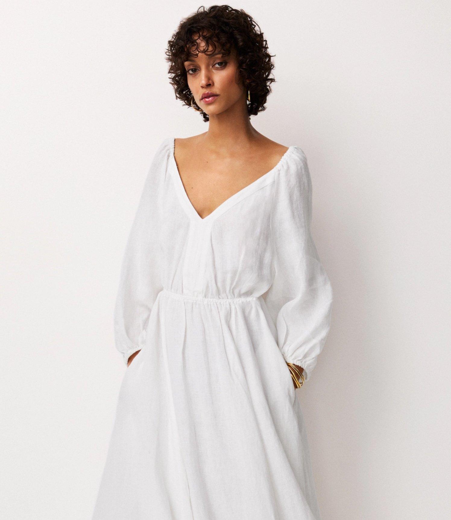 a woman in a white dress standing against a wall