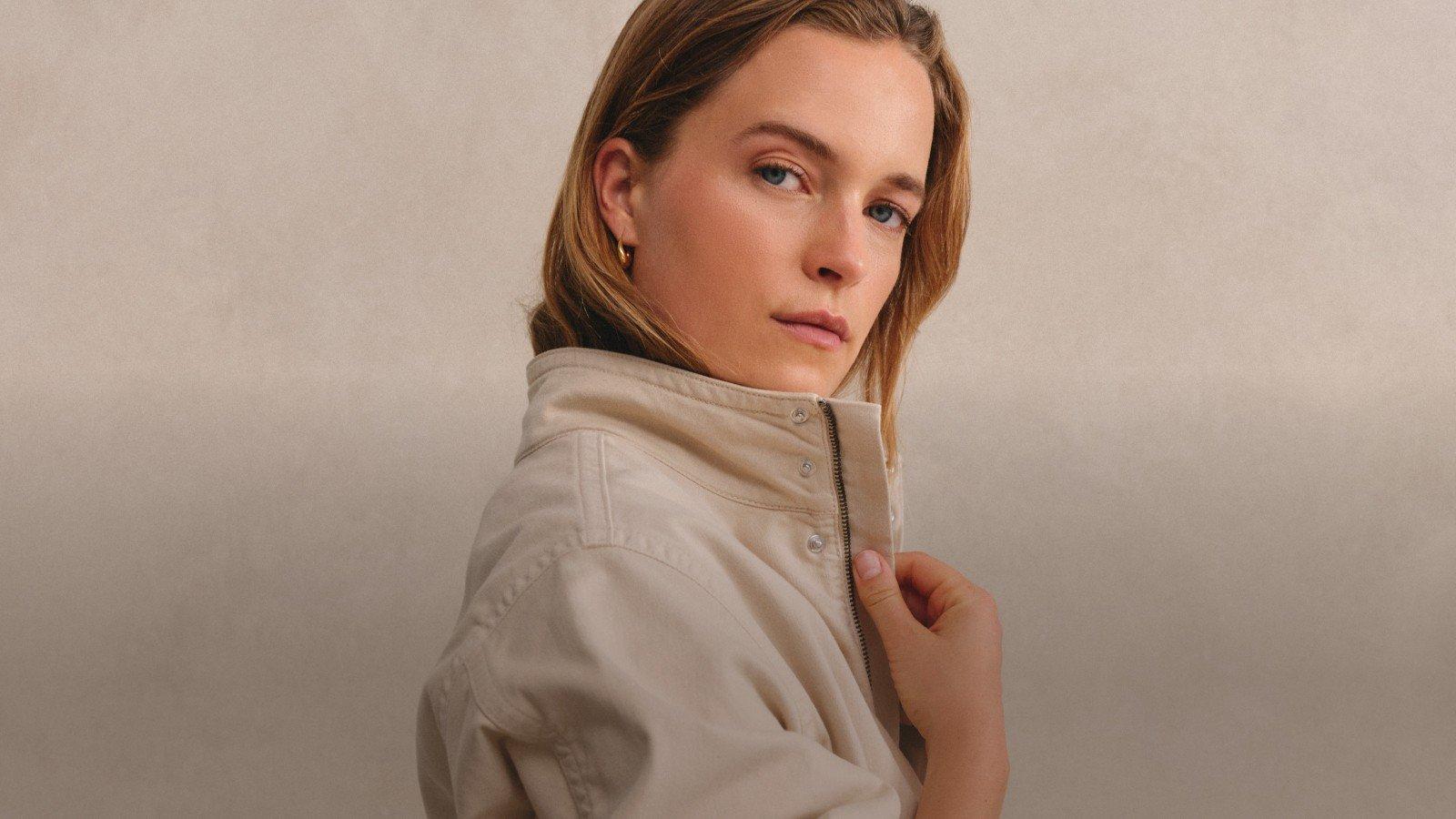 a woman in a beige jacket holding a purse against her shoulder