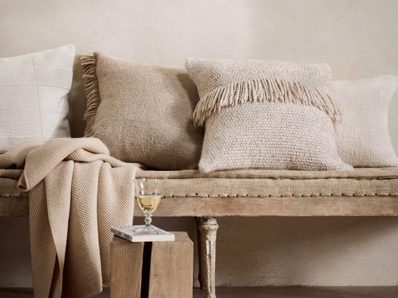 a bench with pillows and blankets on it next to a glass of wine