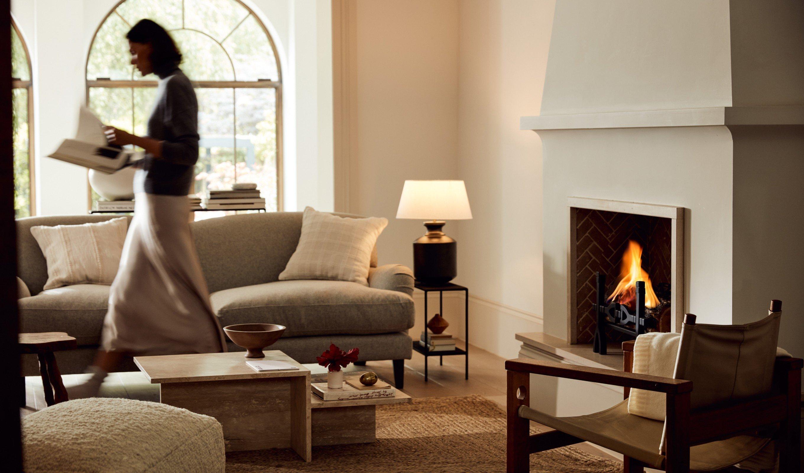 a woman walking through a living room with a fireplace