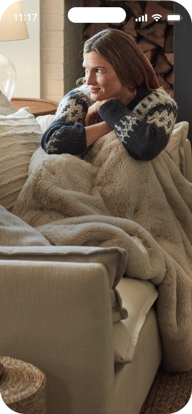 a woman sitting on a couch with a blanket wrapped around her