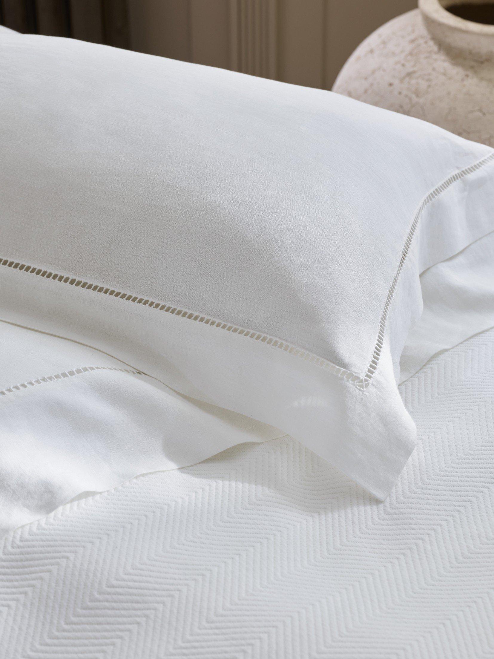 a bed with white sheets and pillows on a white bed