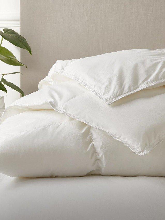 a bed with a white comforter and a plant on top