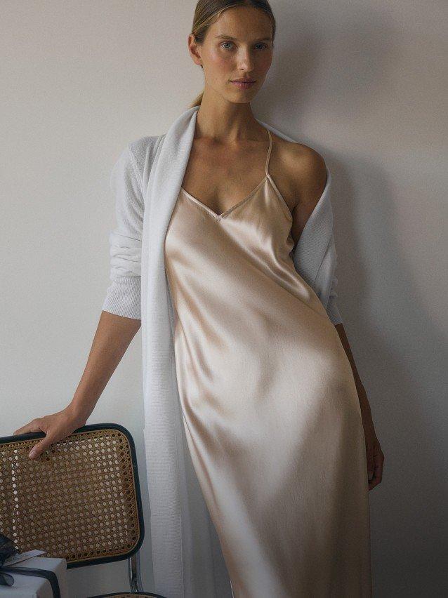 a woman in a long satin dress leaning against a chair