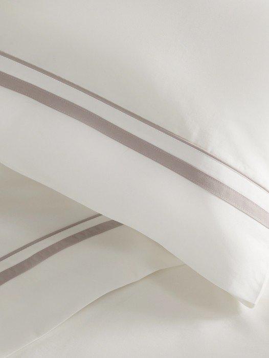 a close up of a bed with white sheets and a silver stripe