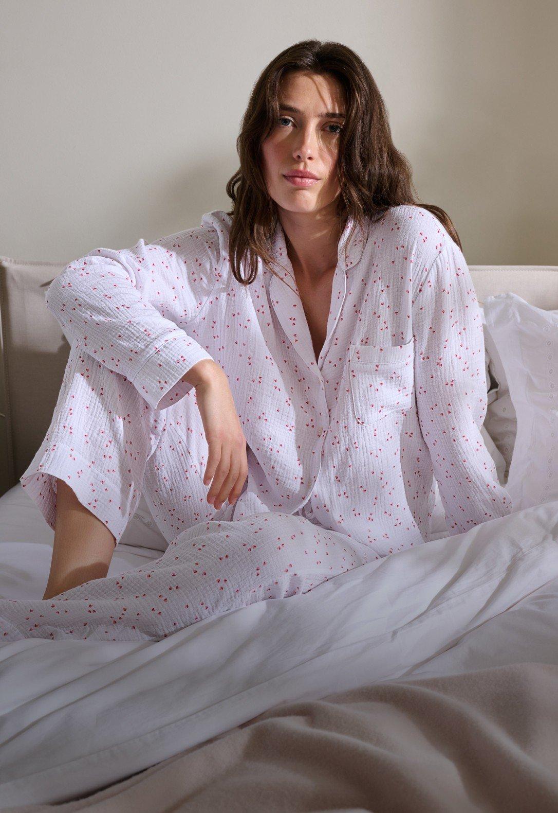 a woman sitting on a bed in a white pajama set