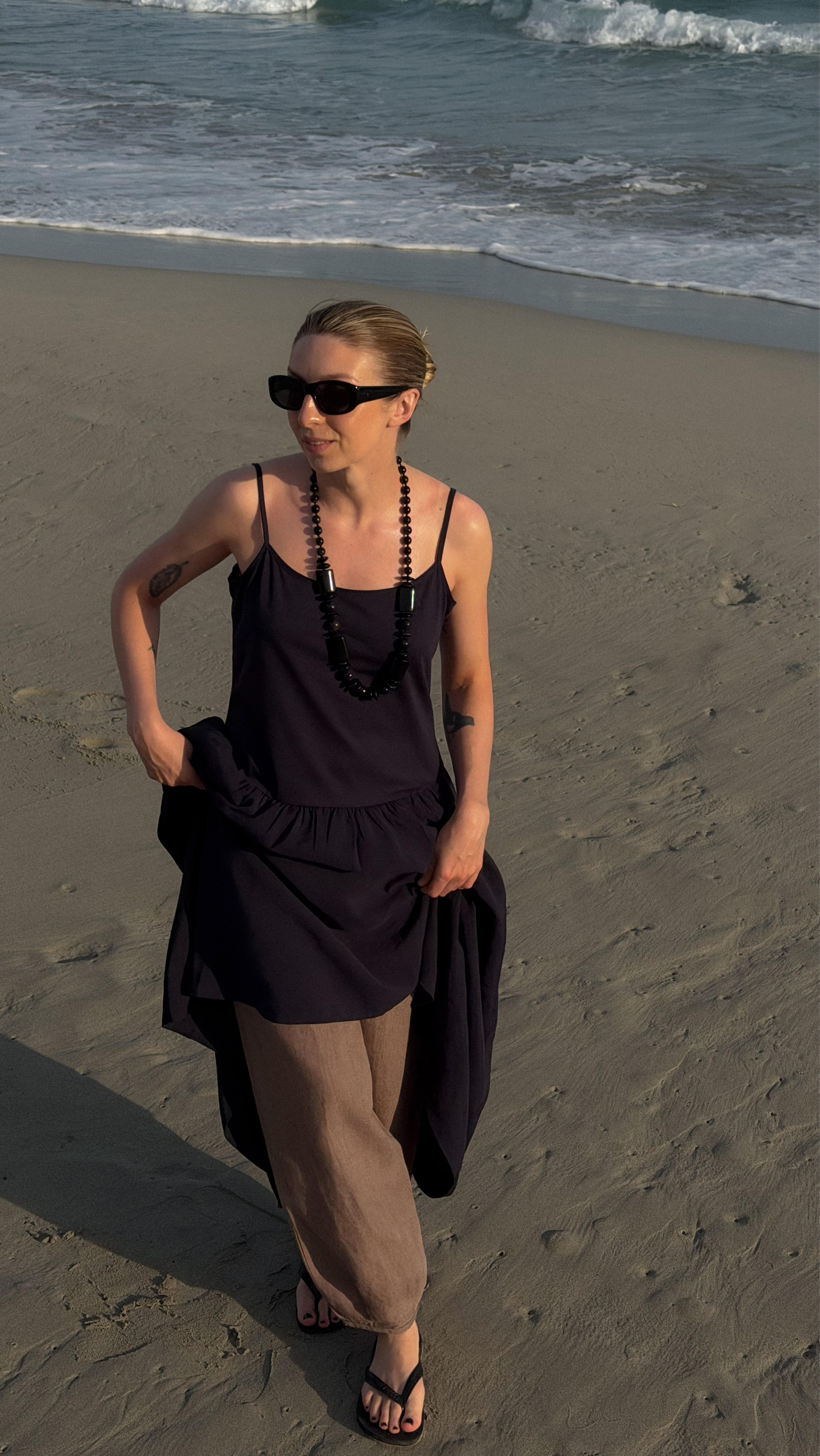 a woman walking on a beach with a hat and sunglasses