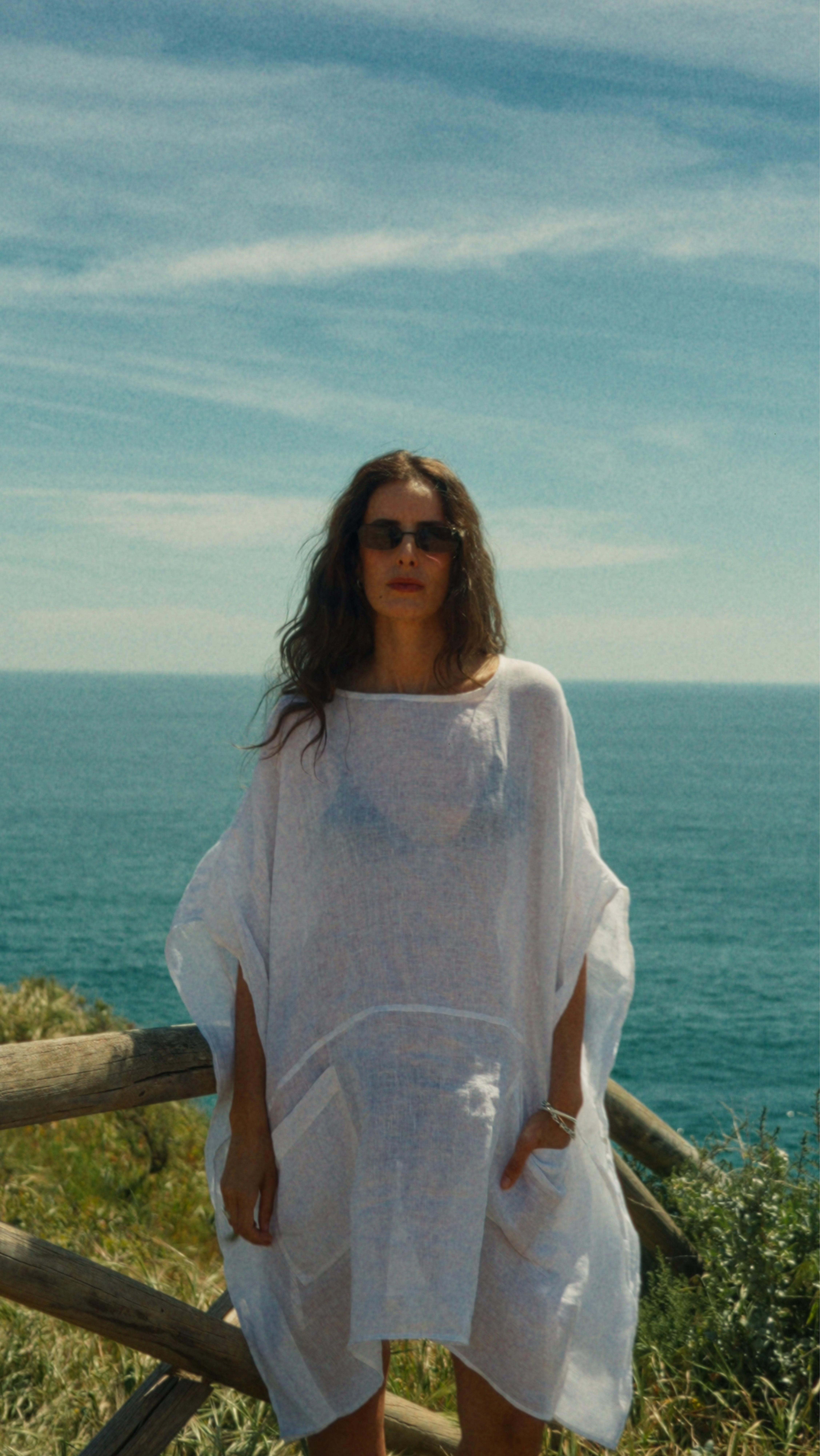 a woman standing on a wooden fence near the ocean