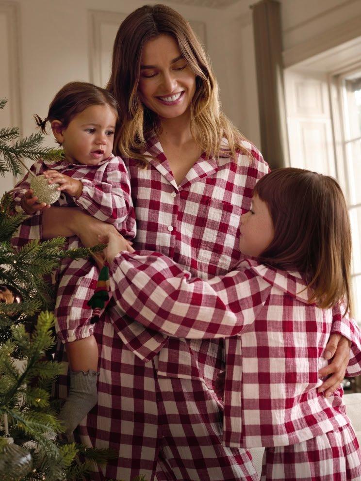 a woman and two children in red plaid pajamas standing next to a christmas tree