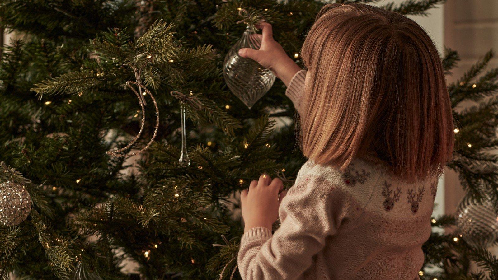 a young girl decorating a christmas tree with ornaments