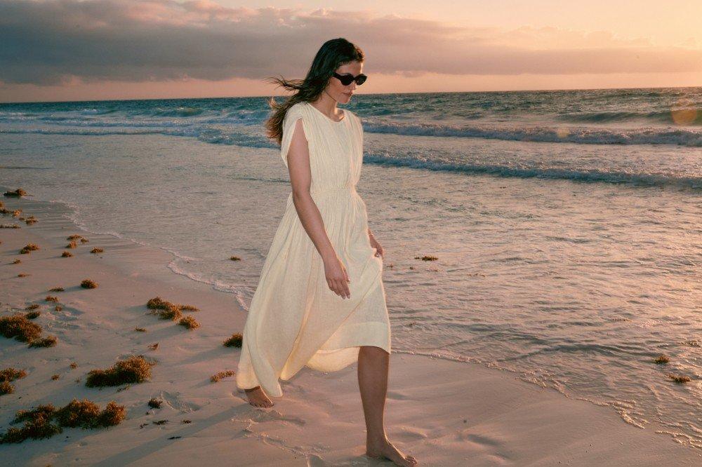a woman in a white dress walking on the beach