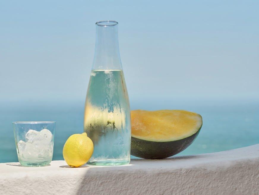a glass of water, lemon and melon on a ledge