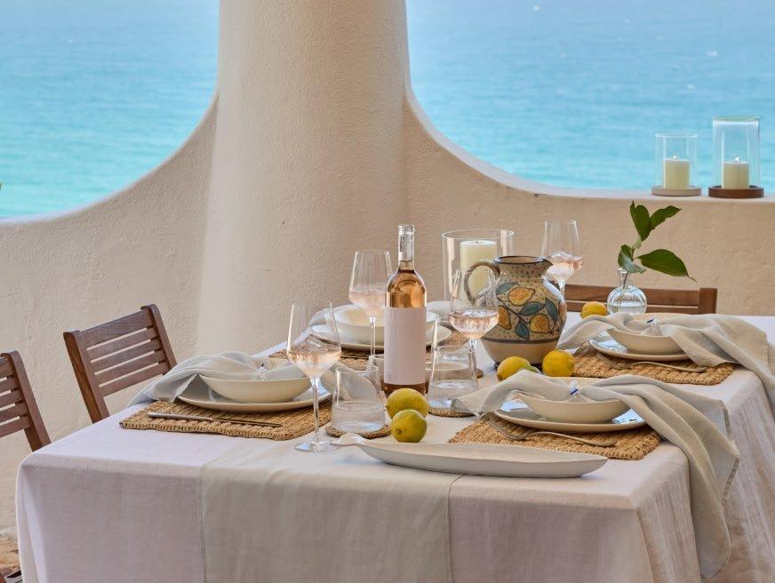 a table set with plates and glasses on a balcony overlooking the ocean
