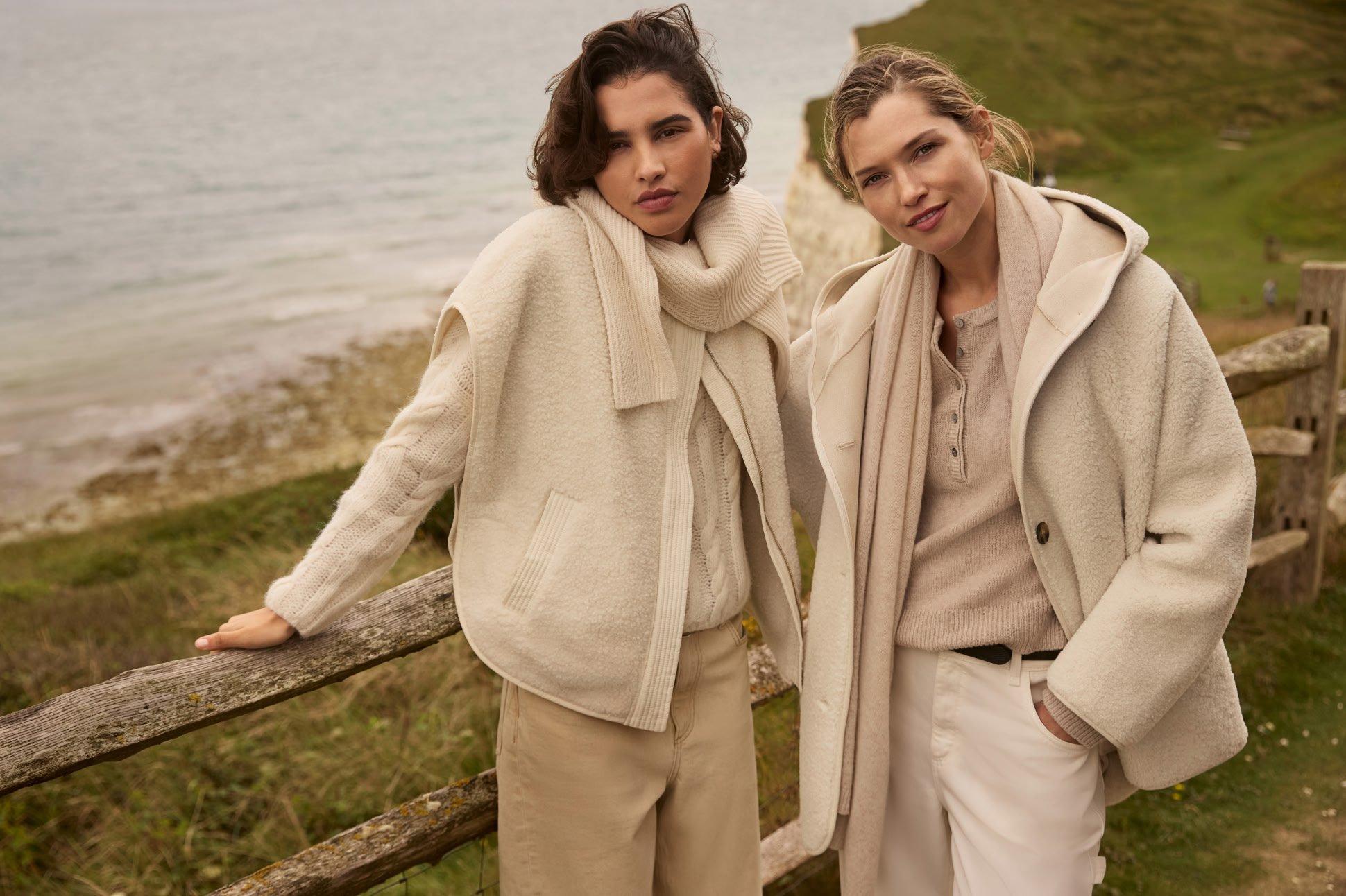 two women in coats standing next to each other on a grassy field