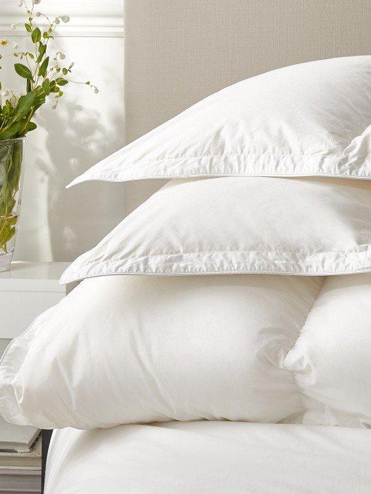 a stack of pillows on a bed with a white vase