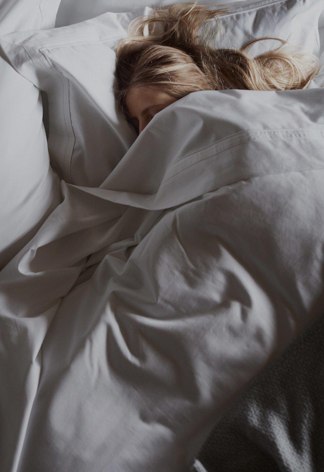 a woman sleeping in a bed with a white sheet