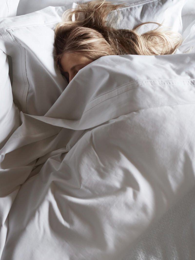 a woman sleeping in a bed with a white sheet
