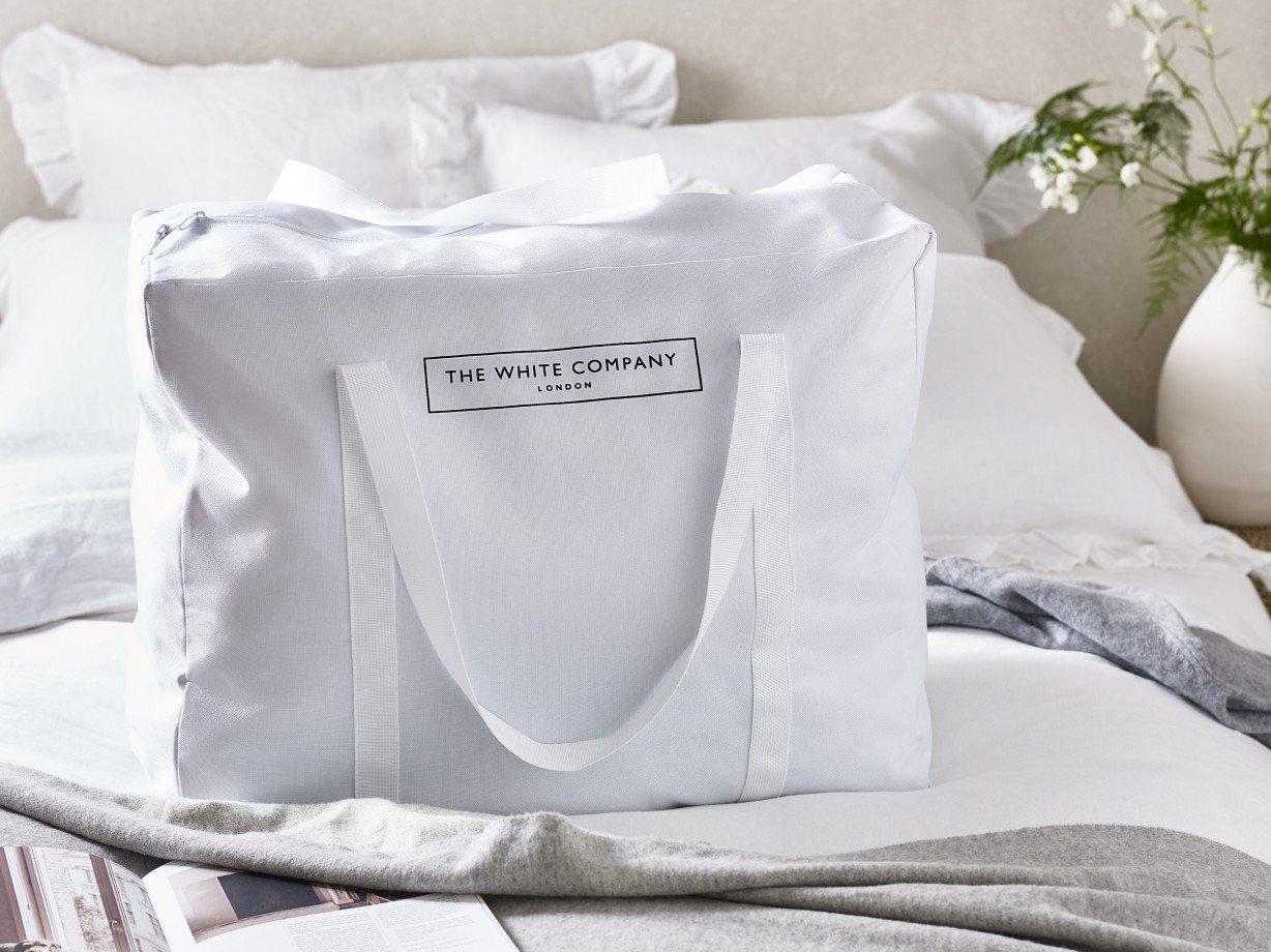 a white bag sitting on top of a bed with a magazine