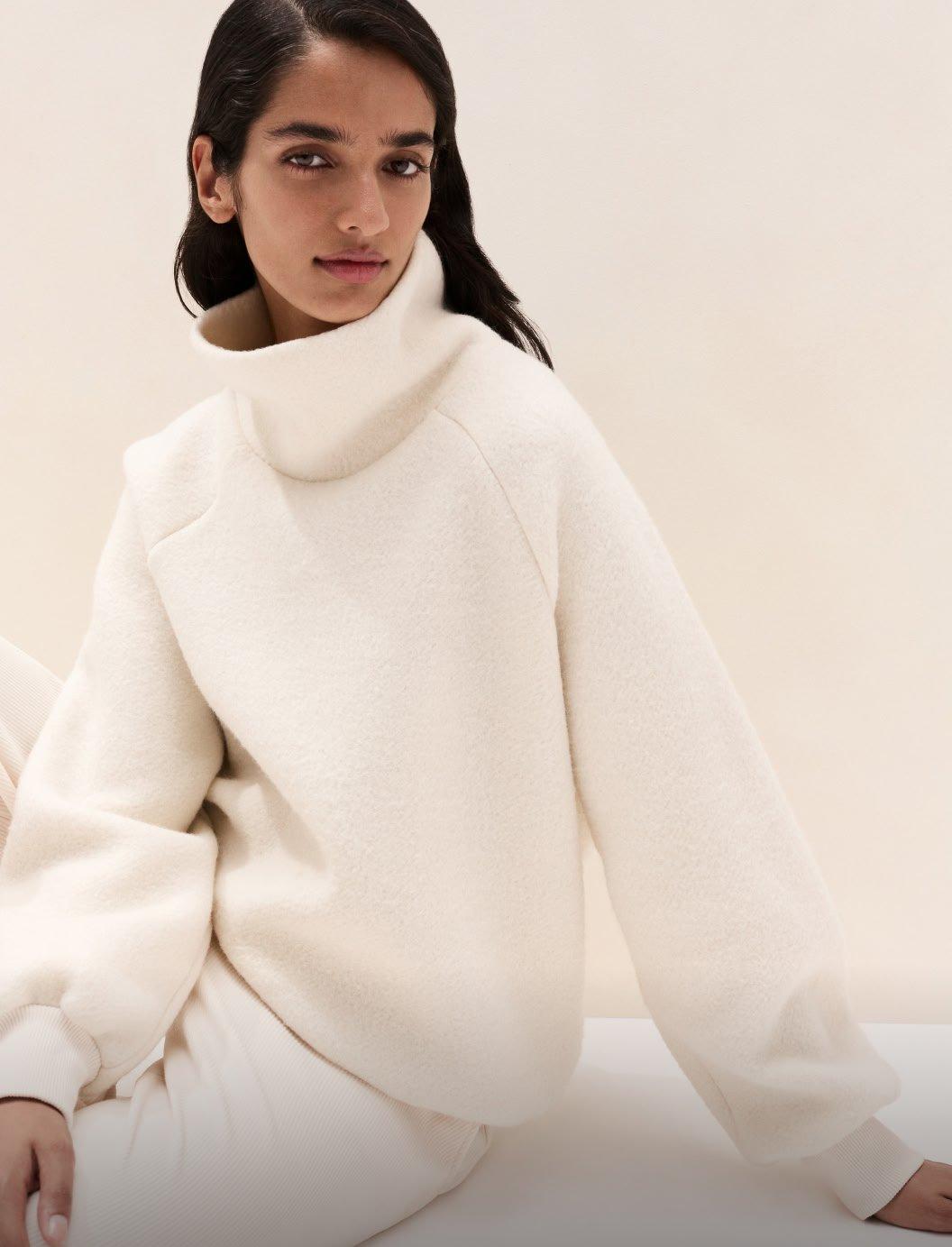 a woman in a white sweater and pants sitting on a white floor
