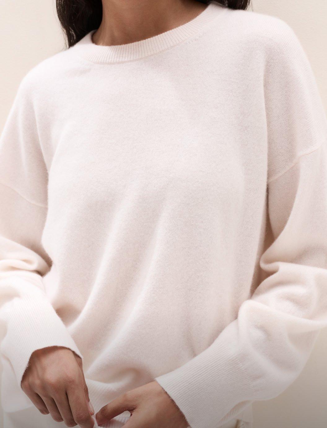 a woman leaning against a wall wearing a beige sweater