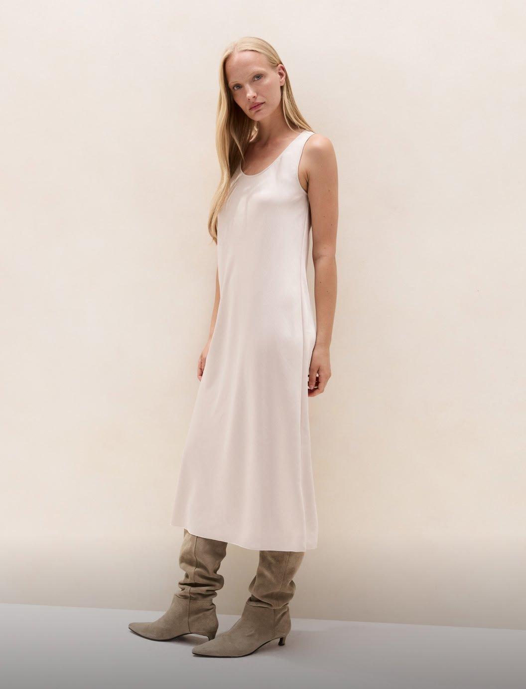 a woman in a white dress and boots standing against a wall