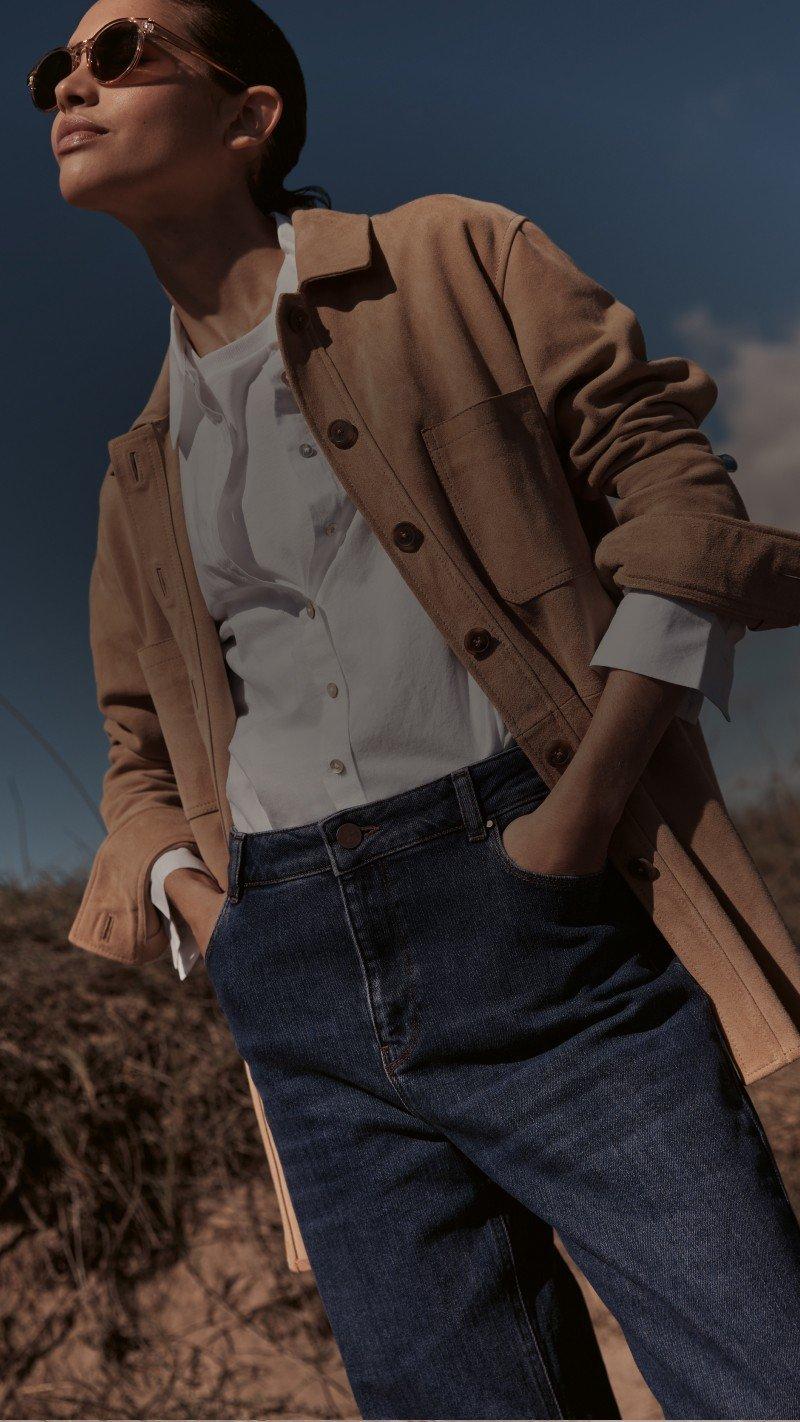 a woman in a jacket and sunglasses standing on a hill