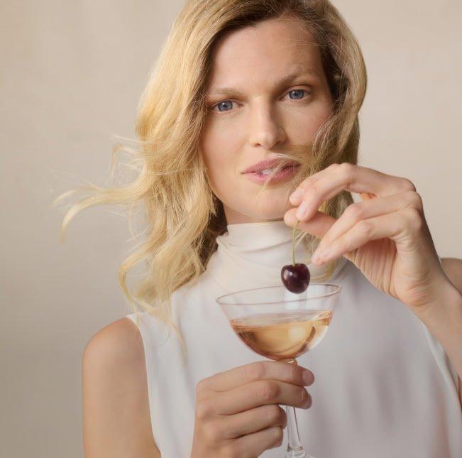 a woman holding a cherry in her hand while holding a glass of wine