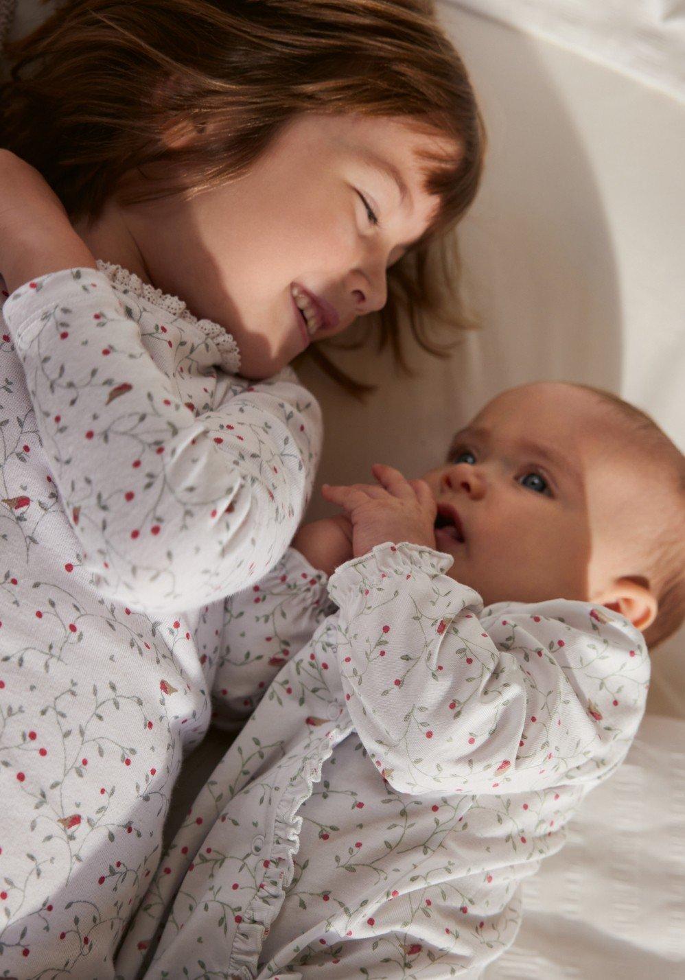 a baby girl and baby boy laying on a bed together