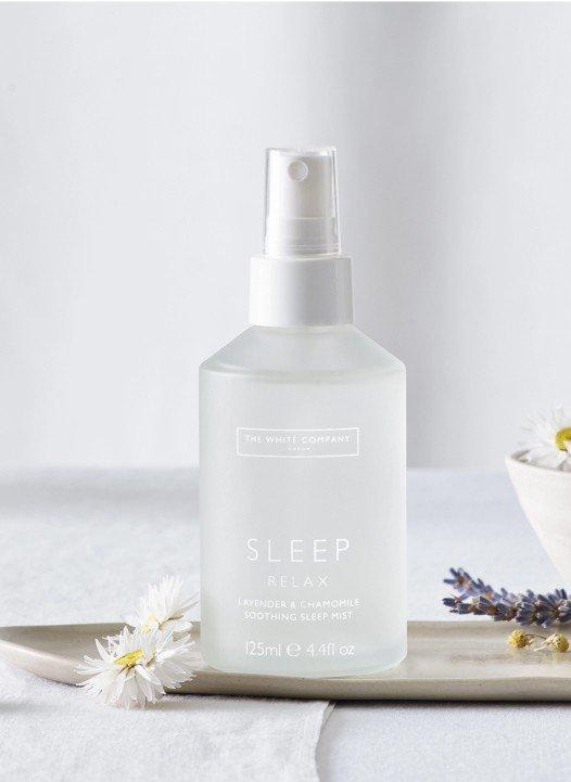 a bottle of a sleep spray sits on a tray with a bowl of flowers