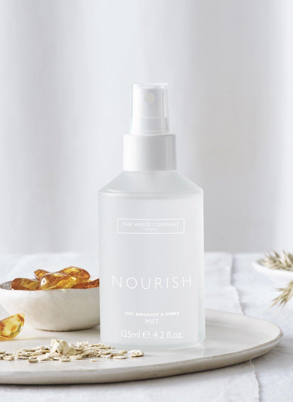 a bottle of nourish spray on a plate next to a bowl of nuts