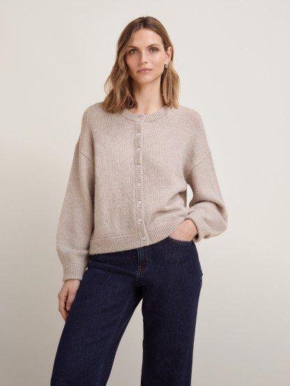 the model wears a light beige cardigan and jeans