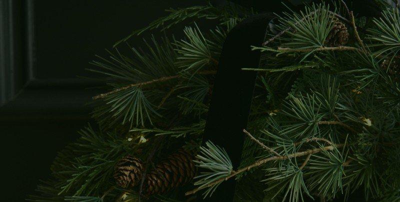 a close up of a wreath with pine cones and a black bow