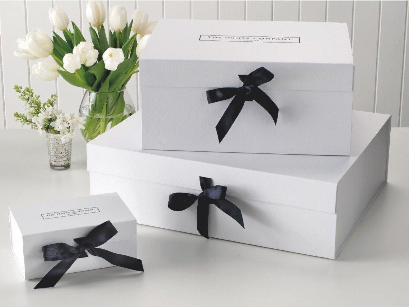 three white boxes with black bows on top of a table