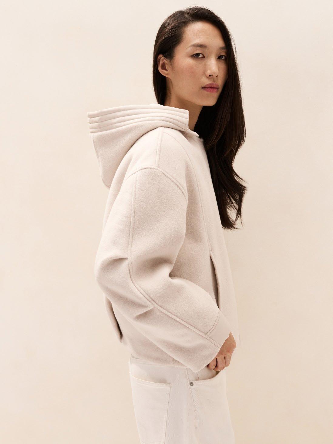 a woman in white sweatshirt and white pants standing against a wall