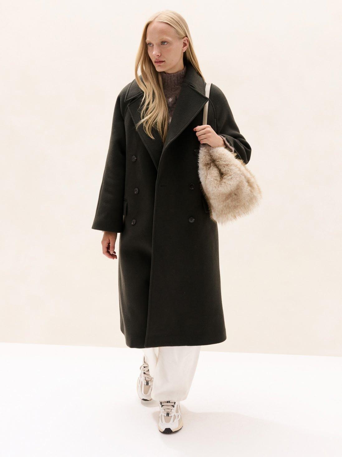 a woman in a black coat and white pants walking
