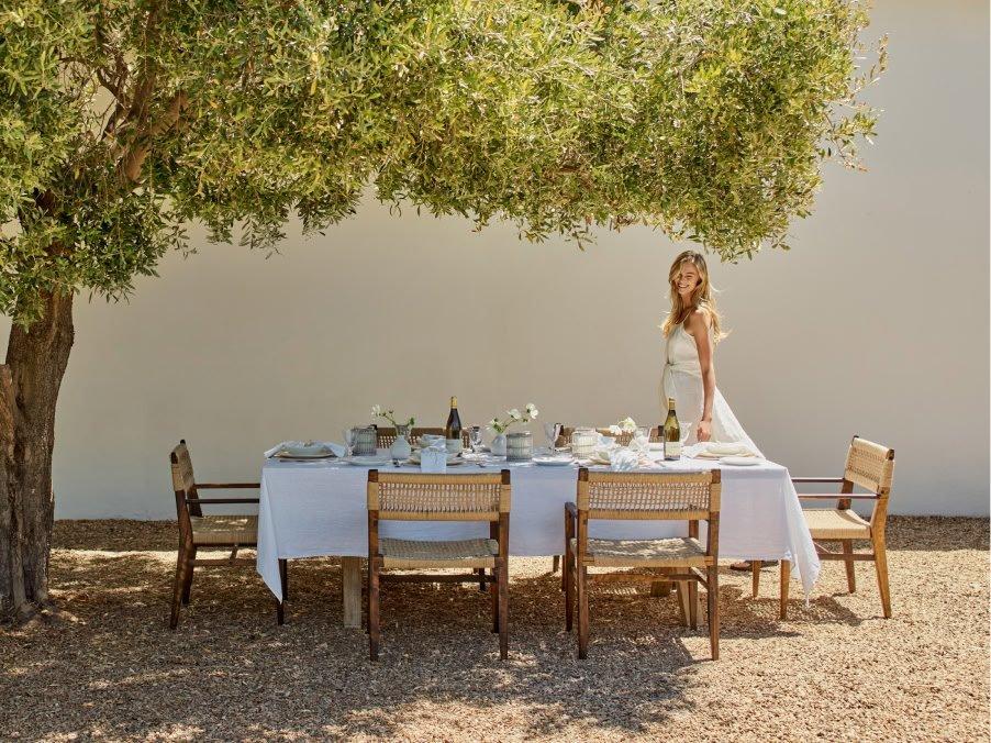a woman standing under a tree with a table set for a dinner party