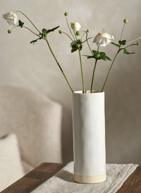 a white vase with flowers on a table in a room