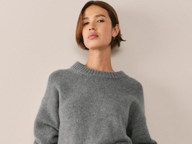 a woman in a grey sweater and white pants posing for a picture