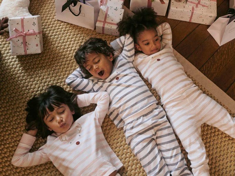 three children in pajamas laying on a carpet in front of a christmas tree