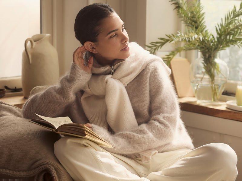 a woman sitting on a chair reading a book while wearing a sweater