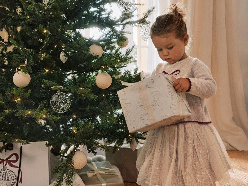 a little girl standing in front of a christmas tree with presents