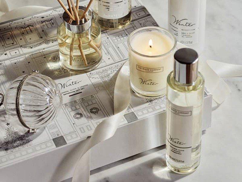 a white table with a bottle of perfume, a candle, and a box of candles