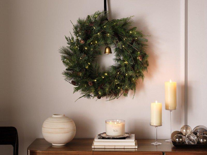 a wreath hanging on a wall next to candles and a vase