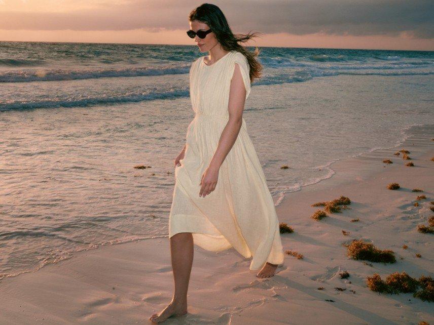 a woman in a white dress walking on the beach