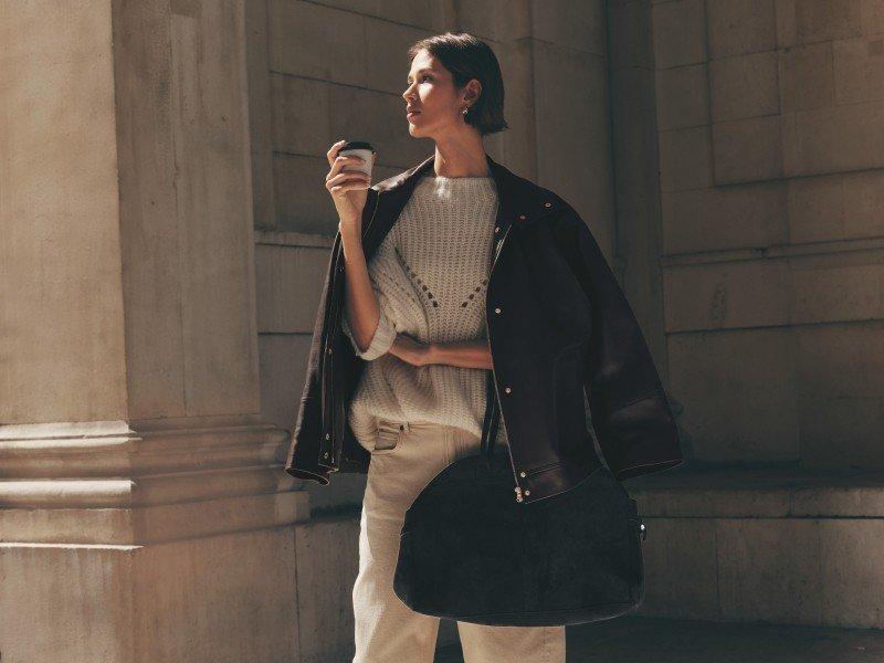 a woman in a black jacket holding a coffee cup