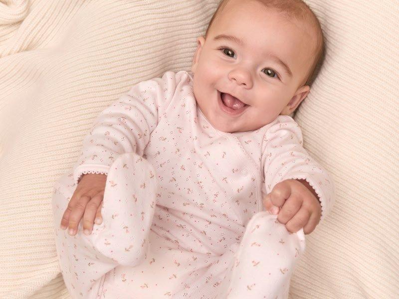 a baby laying on a bed smiling