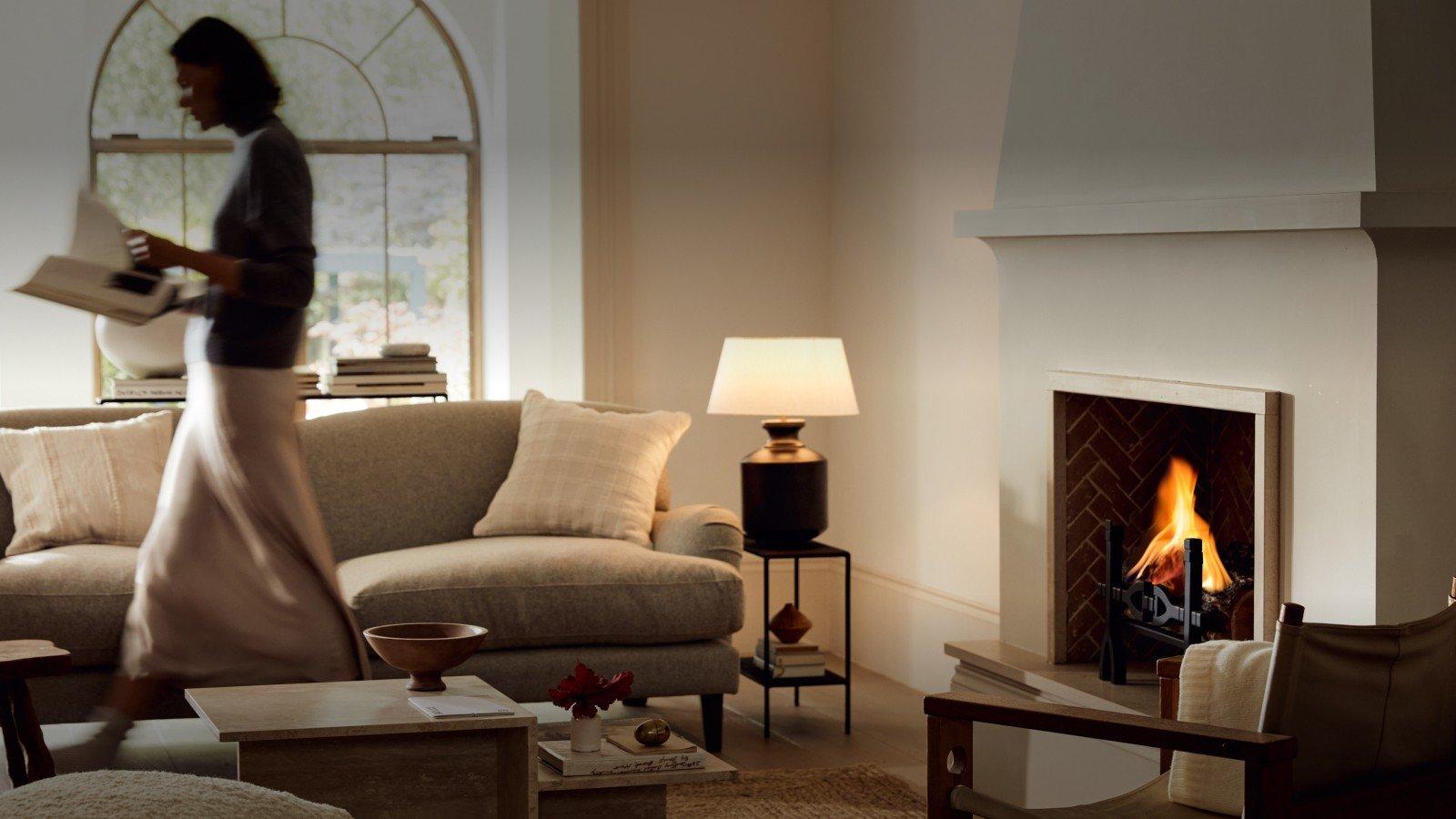 a woman walking through a living room with a fireplace and a couch